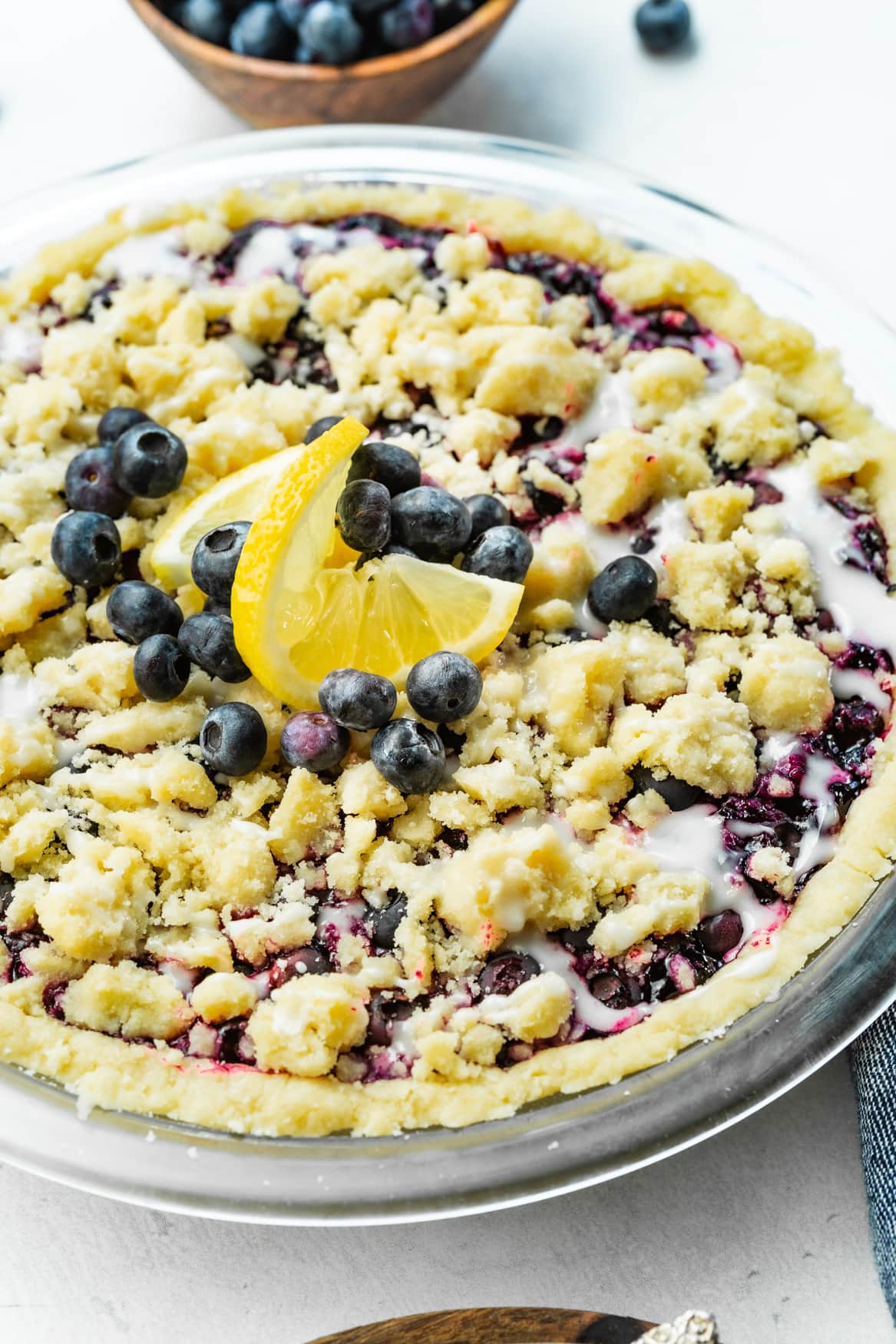a photo of a whole baked wild blueberry pie in a shortbread crust with a streusel topping and a vanilla glaze.