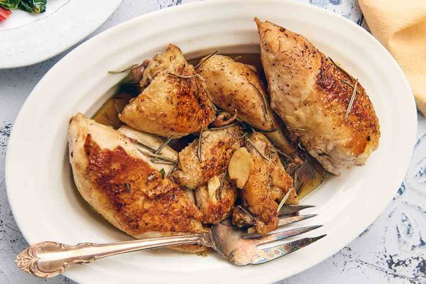 Pieces of chicken being browned in a skillet on a hot plate.