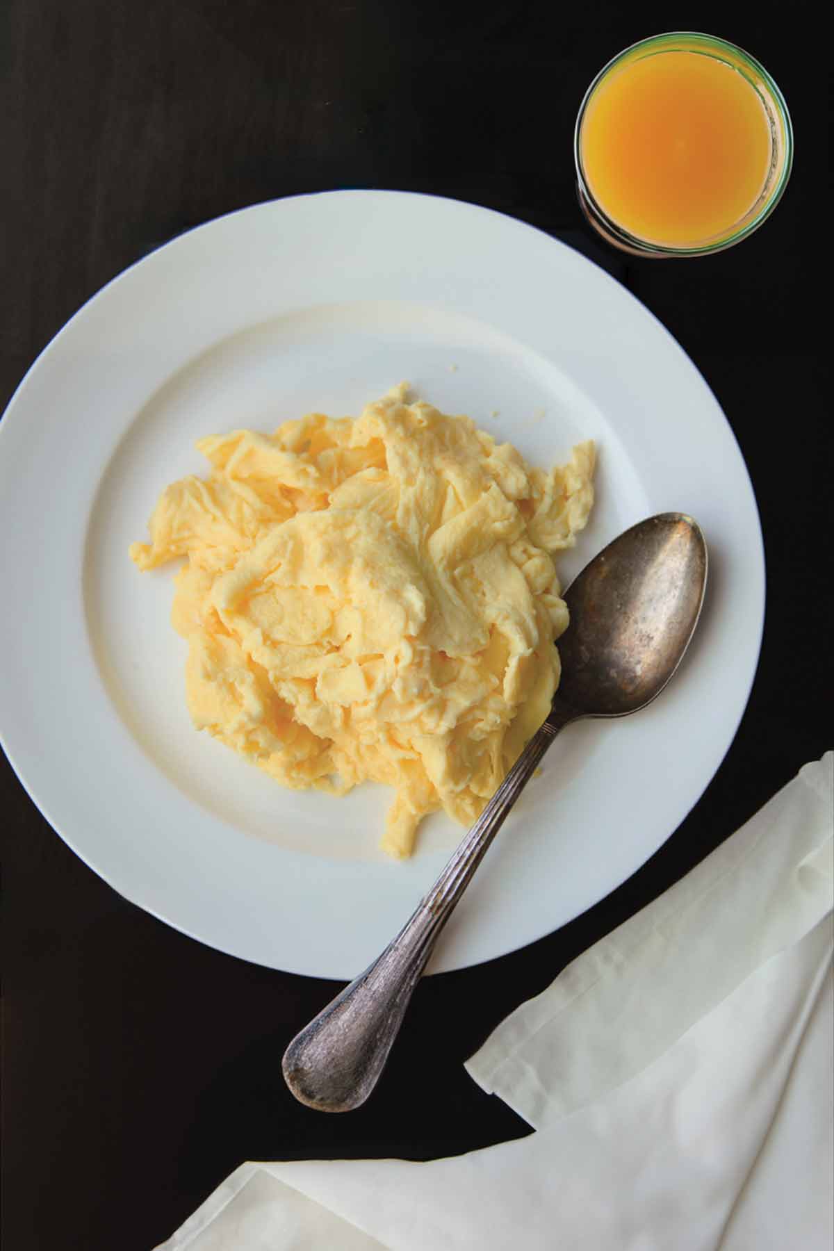 كومة من البيض المخفوق المثالي على طبق أبيض مع ملعقة بجانب البيض.