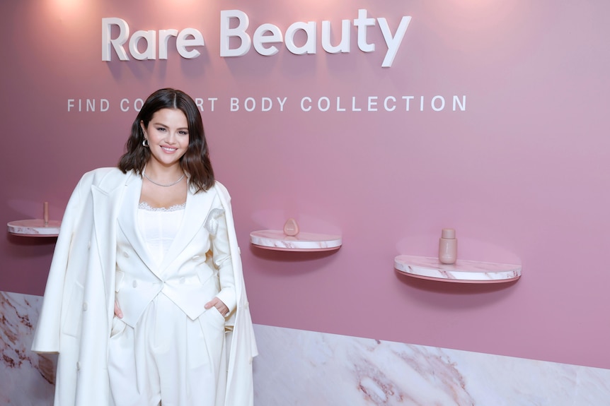 تبتسم سيلينا غوميز بملابس بيضاء بالكامل أمام منتجات مكياج Rare Beauty الخاصة بها في حفل إطلاق المنتج